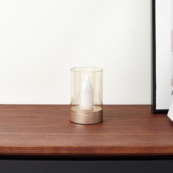 LED-Kerze im Glaszylinder mit goldfarbenem Sockel auf einer Holzoberfläche.