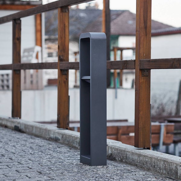 Moderne anthrazitfarbene Außenstandleuchte in schlankem, rechteckigem Design auf einem Steinweg neben einem Holzgeländer.