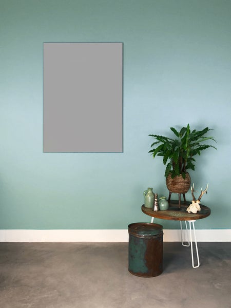 Modern eingerichteter Raum mit mintgrüner Wand, grauem Betonboden und einem runden Holztisch mit Zimmerpflanze neben einer rustikalen Metalltonne.