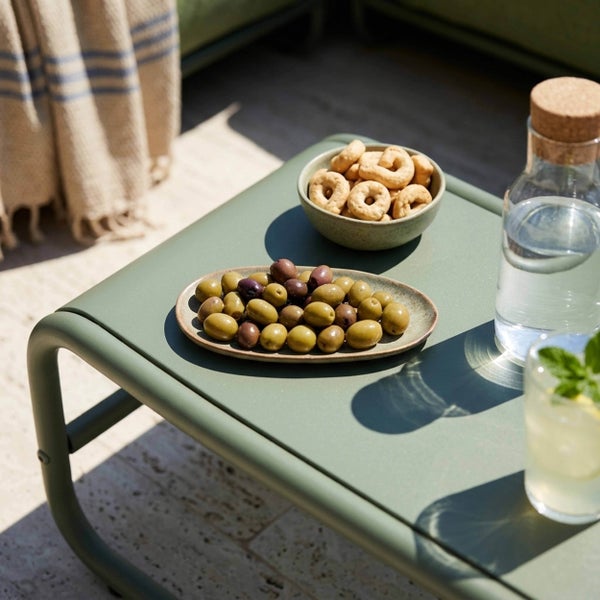 Moderner grüner Gartenbeistelltisch aus Metall mit Oliven, Snacks und Getränken in einer hellen Außenumgebung.
