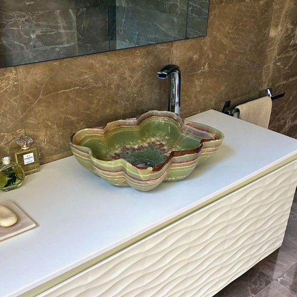 Modernes Badezimmer mit Naturstein-Aufsatzwaschbecken auf weißem Unterschrank mit Wellenstruktur und hoher Chrom-Armatur.
