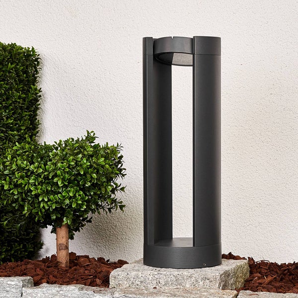 Moderne Pollerleuchte in Anthrazit, platziert auf einem Steinquader in einem Gartenbeet neben kleinen Buchsbäumen.