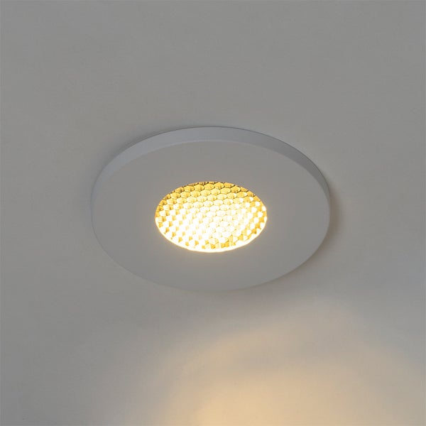 Runder, weißer Einbaustrahler an der Decke mit eingeschaltetem Leuchtmittel in Wabenoptik.
