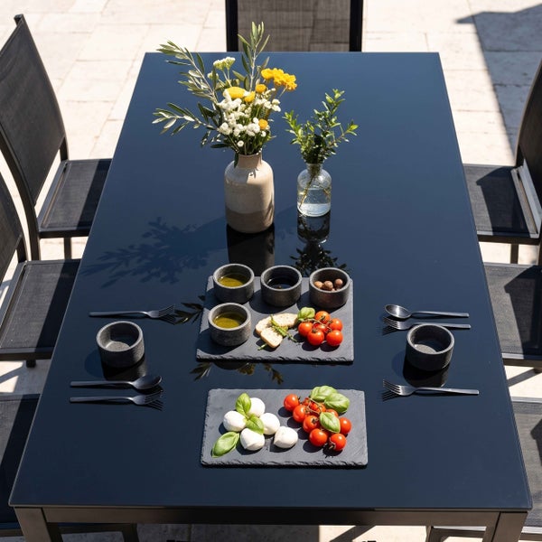 Moderner rechteckiger Gartentisch mit dunkler Glasplatte und passenden Gartenstühlen aus Metall und Textilene auf einer sonnigen Terrasse.
