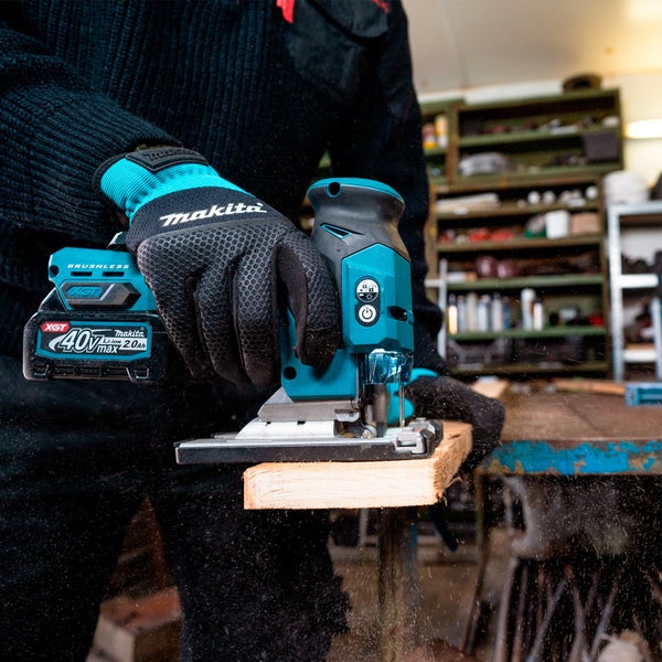 Person mit Makita Handschuhen sägt ein Holzbrett mit einer Makita Akku-Stichsäge 40 Volt max XGT in einer organisierten Werkstatt.