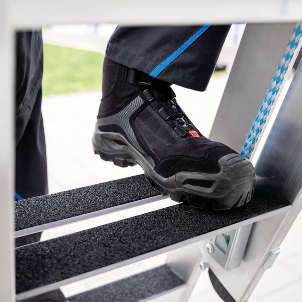 Ein Fuß in einem Sicherheitsschuh auf einer Leiterstufe