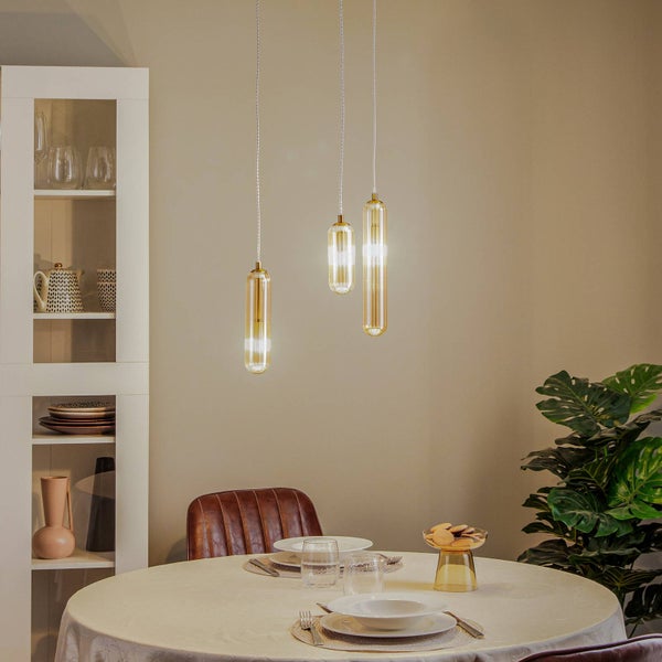 Dreiflammige Pendelleuchte mit zylindrischen Gläsern in Gold über einem gedeckten runden Esstisch in einem modern eingerichteten Zimmer.