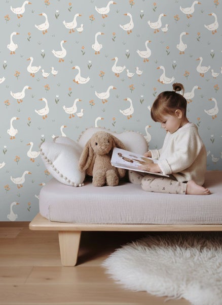 Kind sitzt auf Bett vor Tapete mit Gänsemuster und liest Buch