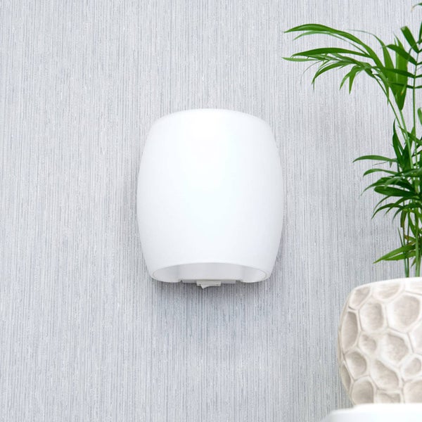 Weiße, gewölbte Wandleuchte aus Glas an einer Wand neben einer Pflanze.