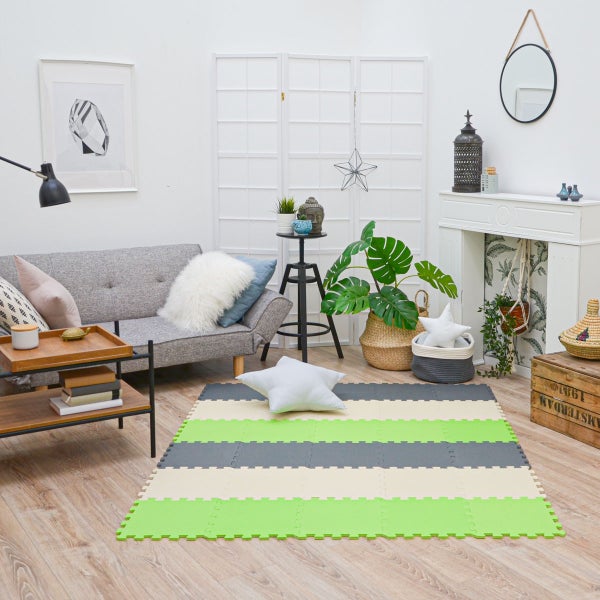 Gestreifte Spielmatte aus Schaumstoff in einem hellen Wohnzimmer mit grauem Sofa und Pflanzen.