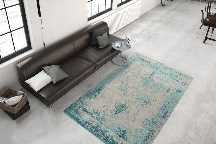 Wohnbereich mit modernem Sofa und einem Vintage Teppich im Used Look in einem hellen, weitläufigen Loft mit Betonboden und großen Fenstern.