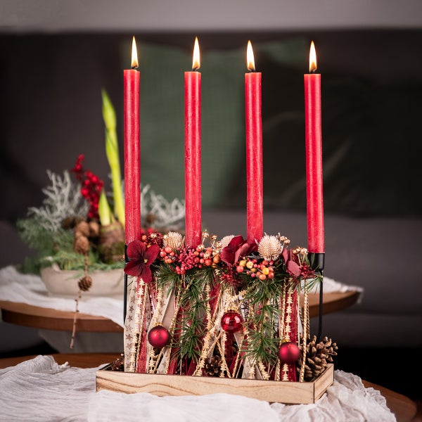 Adventsgesteck mit vier roten Kerzen, weihnachtlicher Dekoration und Holztablett