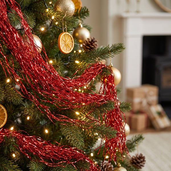 Weihnachtsbaum mit rotem Lametta, Kugeln, Lichterkette und getrockneten Orangenscheiben dekoriert.