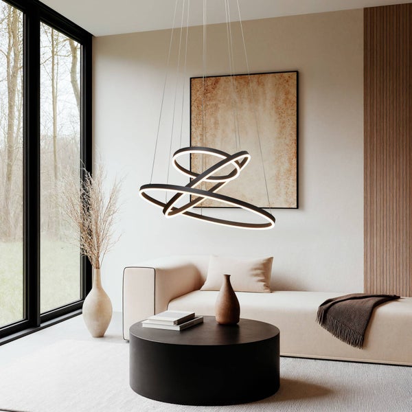 Moderne, schwarze LED-Pendelleuchte in Ringform in einem hellen, minimalistischen Wohnzimmer mit Sofa und großem Fenster.