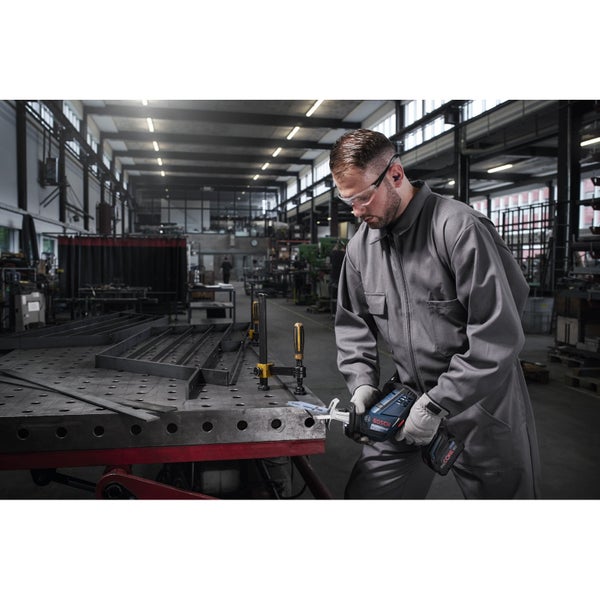 Ein Mann in Arbeitskleidung sägt mit einer Akku-Säbelsäge Metall auf einer Werkbank in einer Werkstatt.