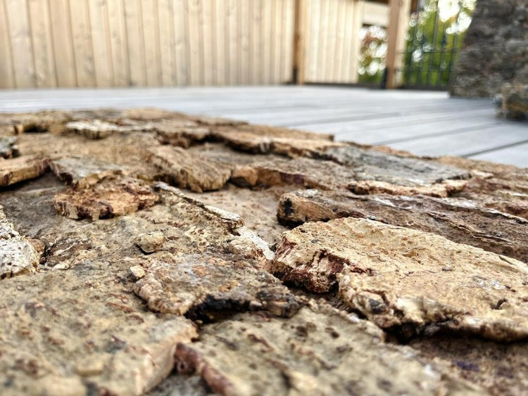 Nahaufnahme von Wandverkleidung aus Naturkork mit rauer Rindenstruktur auf einer hellen Holzterrasse.