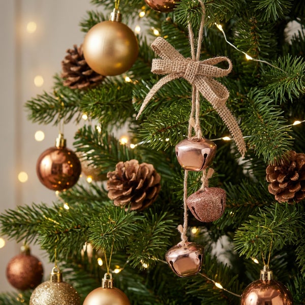 Weihnachtsbaum geschmückt mit Kugeln, Tannenzapfen und einem Glockenanhänger mit Juteschleife bei Lichterkettenbeleuchtung.