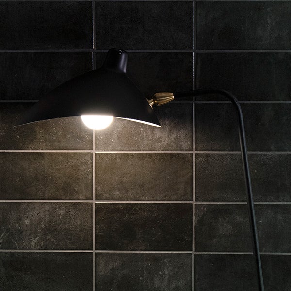 Moderne Stehleuchte mit gebogenem Arm und schirmartigem Leuchtenkopf vor einer gefliesten Wand
