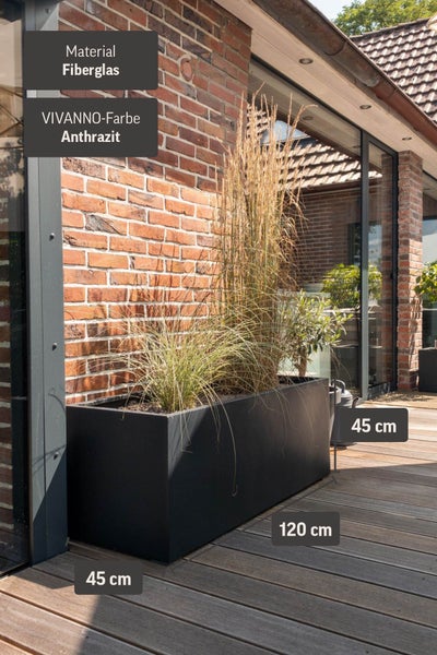 Vivanno Pflanztrog aus Fiberglas in Anthrazit auf einer Holzterrasse vor einer Ziegelwand, Maße 120 mal 45 mal 45 Zentimeter.