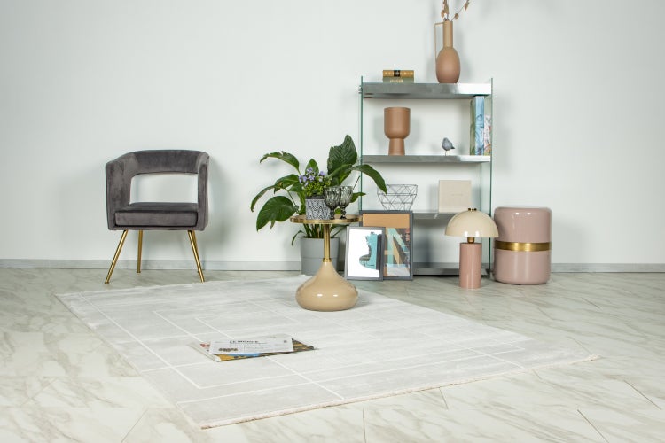 Modernes Wohnzimmer mit samtigem Stuhl, rundem Beistelltisch, Glasregal, Tischlampe, Dekoobjekten und einem gemusterten Teppich auf Marmorboden.