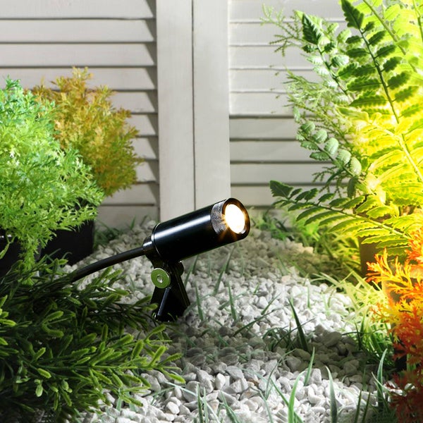 Kleiner schwarzer LED-Gartenstrahler beleuchtet Pflanzen in einem Beet mit Kies.