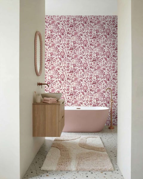 Badezimmer mit florale Tapete hinter einer freistehenden Badewanne, kombiniert mit einem Holzwaschtisch und einem runden Spiegel.