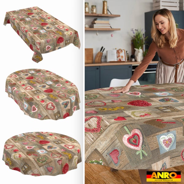 Abwaschbare Tischdecke mit Holzoptik und Herzmotiven in rechteckig, oval und rund. Frau legt Decke in Küche auf. ANRO Deutsche Manufaktur Logo.