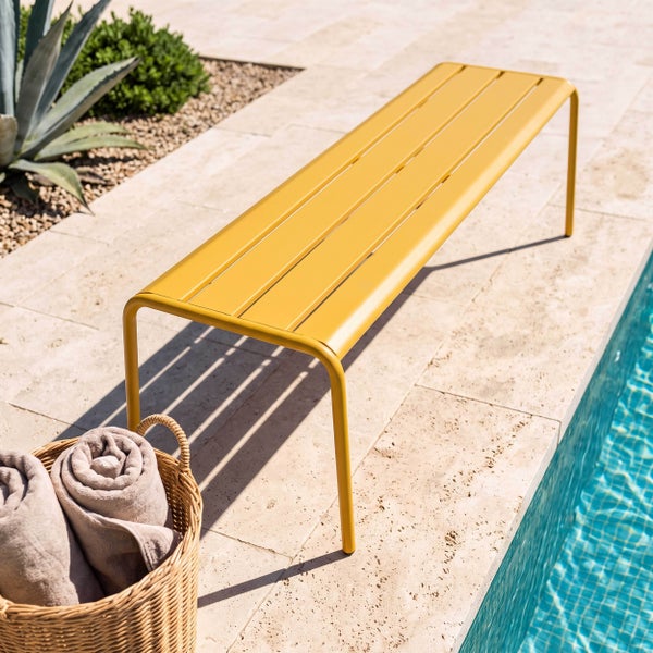 Moderne Gartenbank aus Metall mit Lattenstruktur auf einer Terrasse aus Stein neben einem Pool.