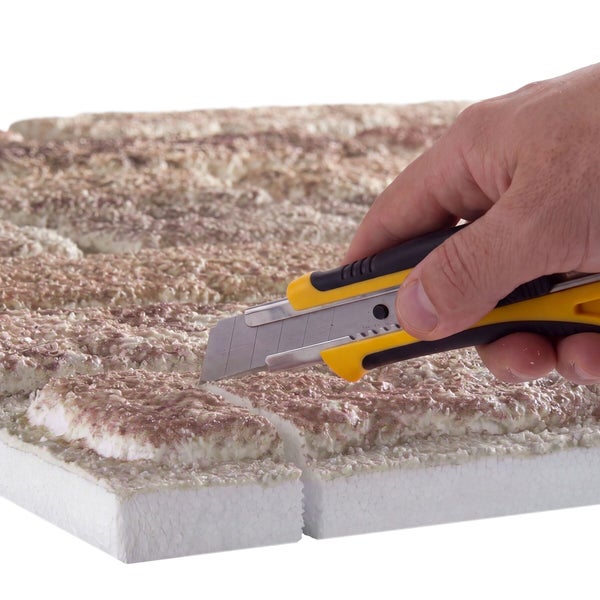 Hand schneidet mit einem Cuttermesser eine Dämmplatte aus Polystyrol zu
