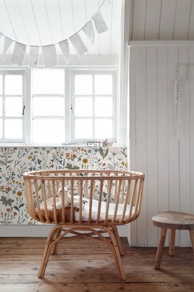Kinderzimmer mit Babybett, floraler Tapete und Holzfußboden für eine helle und freundliche Atmosphäre.