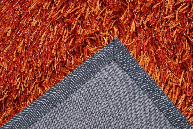 Detailansicht eines orangefarbenen Hochflor-Teppichs mit sichtbarem grauem Teppichrücken.
