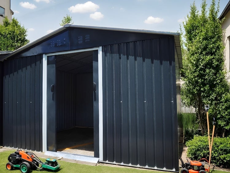 Geräumiges Gartenhaus aus Metall in Anthrazit mit Satteldach und offener Schiebetür in einem Garten mit Rasen und Gartengeräten.