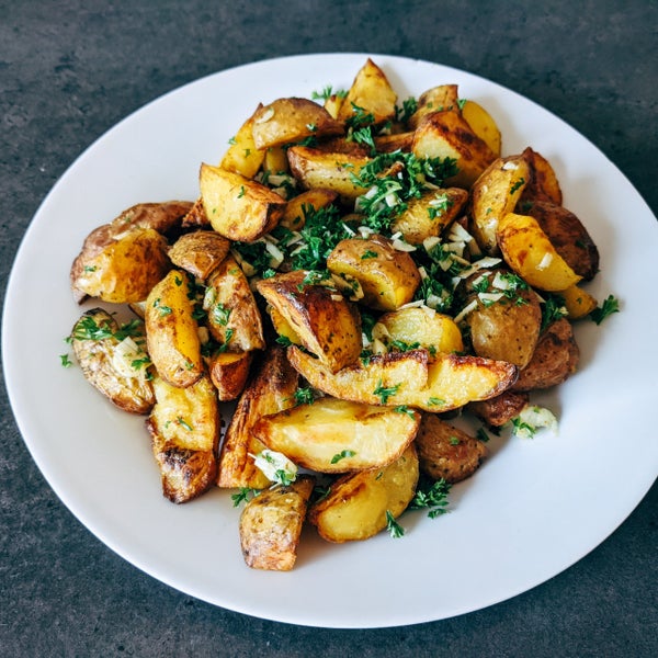 Geröstete Kartoffelspalten mit Petersilie und Knoblauch auf einem Teller.