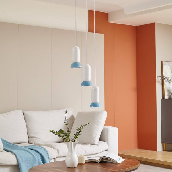 Moderne dreiflammige Pendelleuchte in Weiß und Blau in verschiedenen Höhen in einem hellen Wohnzimmer mit Sofa und Holztisch.