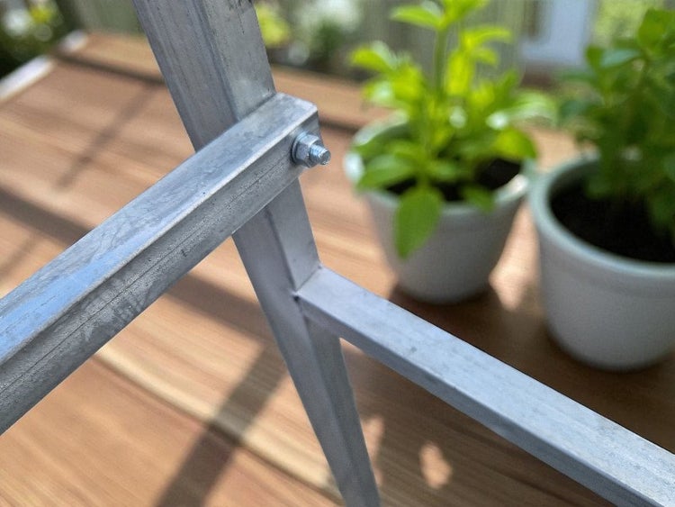 Detailansicht eines Metallgestells mit Schraubverbindung und Pflanzen im Hintergrund