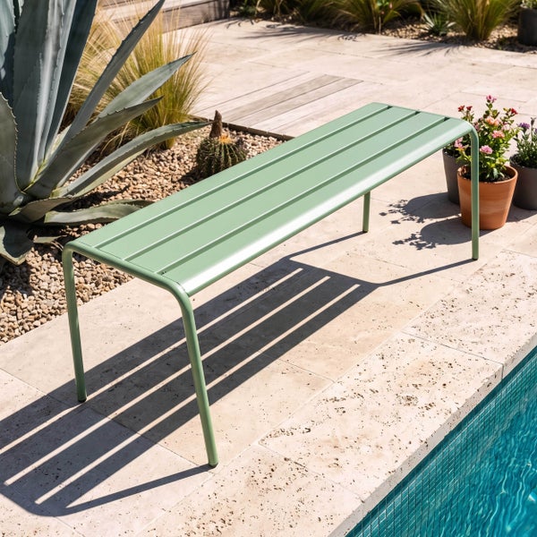 Grüne Gartenbank aus Metall auf einer hellen Steinterrasse neben einem Pool, umgeben von mediterranen Pflanzen.