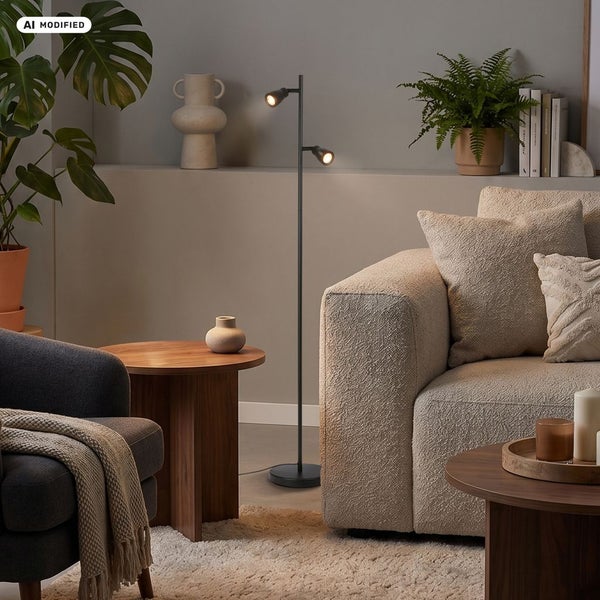 Moderne Stehlampe mit zwei schwenkbaren Spots in einem gemütlich eingerichteten Wohnzimmer mit Sofa und Pflanzen.