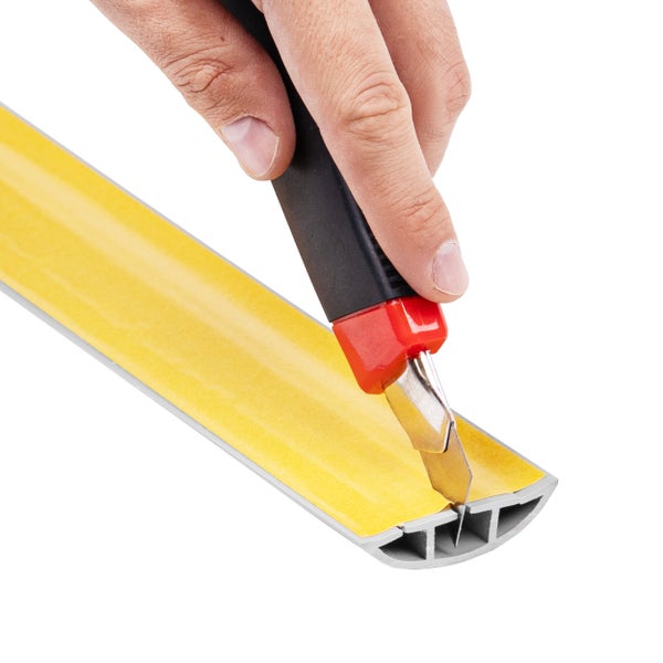 Eine Hand schneidet mit einem Cuttermesser die Schutzfolie einer selbstklebenden Kabelschiene aus Kunststoff zu.