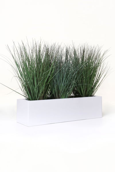 Künstliches Gras in weißem, rechteckigem Pflanzkasten.