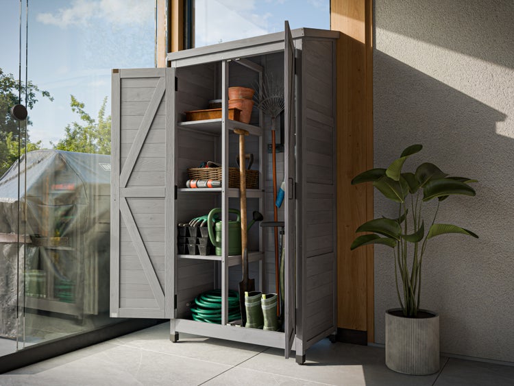Grauer Gartenschrank aus Holz mit zwei Türen, befüllt mit Gartengeräten wie Harke, Schaufel und Gießkanne auf einer hellen Terrasse.