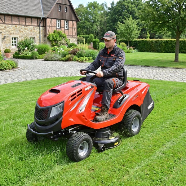 Mann fährt einen roten Rasentraktor auf einer Rasenfläche.