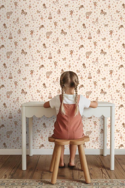 Kindertapete mit Zirkusmotiven wie Tieren und Sternen in einem Kinderzimmer mit Kind an einem kleinen Schreibtisch.