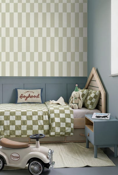 Kinderzimmer mit karierter Tapete, Holz-Hausbett, grün-weißer Bettwäsche, blauem Nachttisch und hellem Rutschauto vor einer Wandpaneele.