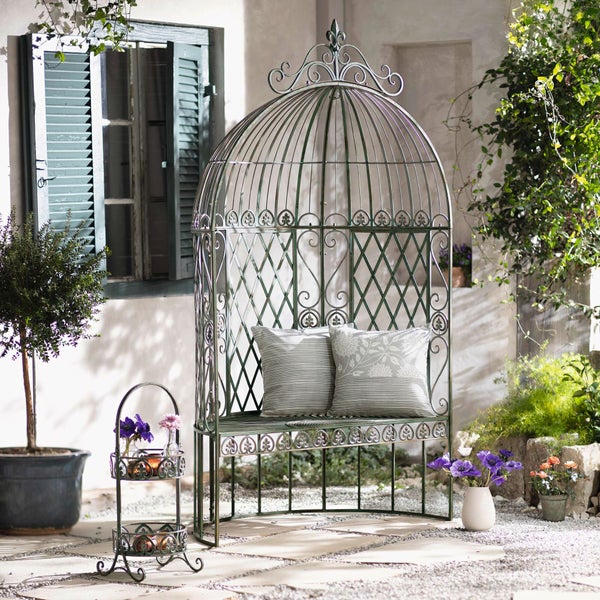 Gartenmöbel-Szene mit einer Metall-Gartenbank, dekoriert mit Kissen, neben einem kleinen Beistelltisch mit Blumen