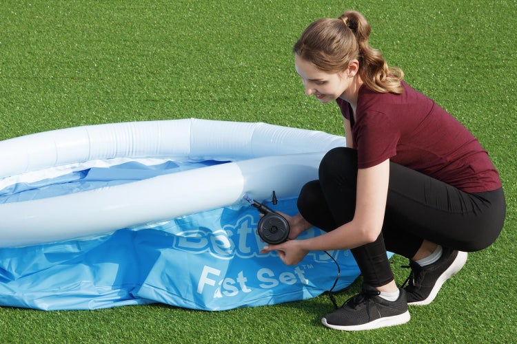 Eine Frau pumpt den oberen Luftring eines Bestway Fast Set Pools mit einer elektrischen Luftpumpe auf einer Rasenfläche auf