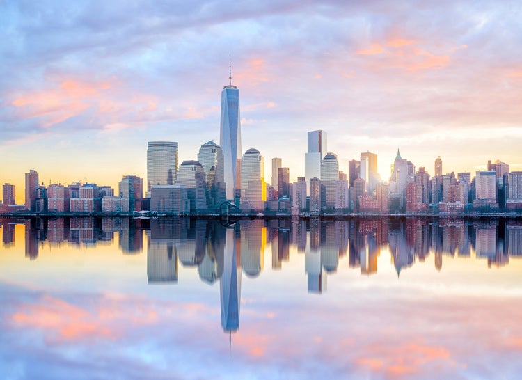 Fototapete mit der Skyline von New York City bei Sonnenuntergang, dem One World Trade Center und Spiegelungen im Wasser.