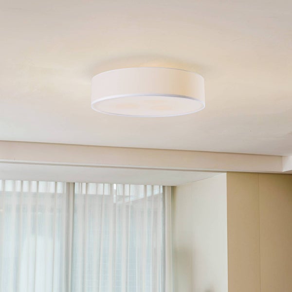 Moderne, runde Deckenleuchte mit weißem Stoffschirm und Diffusor in einem hellen Raum mit transparenten Vorhängen.