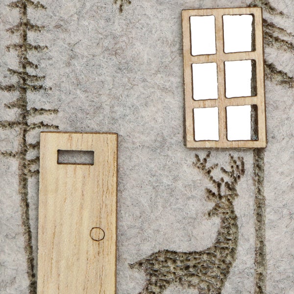 Detailansicht einer Winterdekoration mit Holztür, Fenster und Hirschmotiv auf Filz