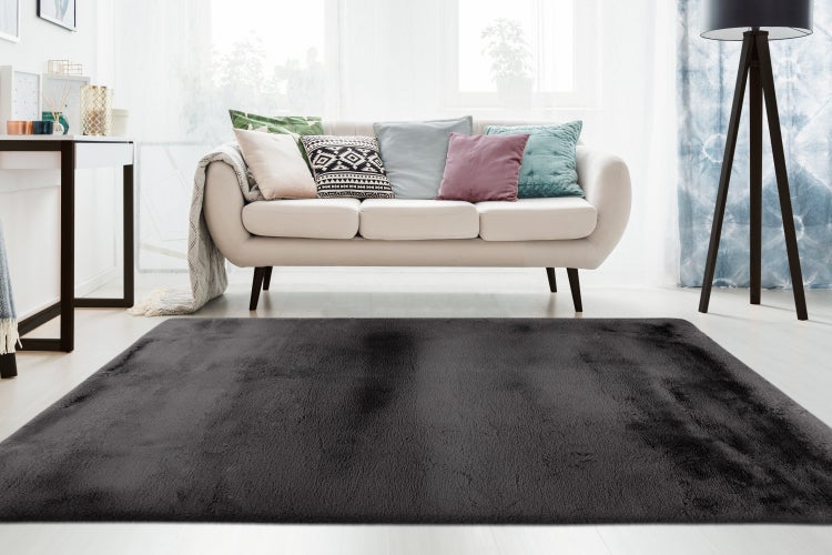 Ein rechteckiger, flauschiger Hochflorteppich vor einem hellen Sofa in einem modern eingerichteten Wohnzimmer.