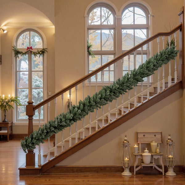 Festlich geschmücktes Treppengeländer aus Holz mit einer grünen Tannengirlande, Laternen und Kerzen im hellen Eingangsbereich.